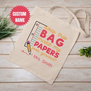 May include: A beige tote bag with a pink, red, and blue graphic that says "Does this bag make my papers look graded?" with a ruler and pencil illustration. The text "Mrs. Smith" is below the graphic.