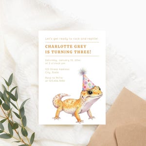 K&ouml;nnte beinhalten: Eine Geburtstagseinladung mit einer Aquarellillustration eines Geckos mit Partyhut. Die Einladung lautet "CHARLOTTE GREY WIRD DREI!" mit Veranstaltungsdetails. Enth&auml;lt einen hellbeige Umschlag und Eukalyptuszweige.