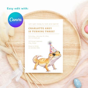 K&ouml;nnte beinhalten: Eine Geburtstagseinladung mit einem Aquarell-Gecko, der einen Partyhut tr&auml;gt. Der Einladungstext lautet "CHARLOTTE GREY WIRD DREI!" mit Veranstaltungsdetails. Die Einladung befindet sich auf einem Holztablett mit dekorativen Elementen.