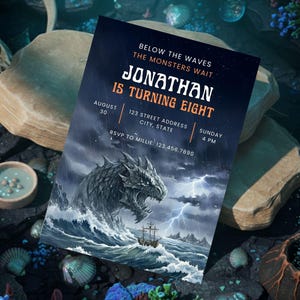 Op de afbeelding: Een donkerblauwe uitnodiging met de tekst "JONATHAN IS TURNING EIGHT" en evenementdetails. Het ontwerp toont een draak die uit stormachtige golven oprijst, met een schip in de verte. De uitnodiging is omgeven door decoratieve elementen.