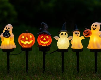 Może przedstawiać: Szereg podświetlanych dekoracji na Halloween, w tym duchy i dynie, na czarnych palikach. Świecące figury są pomarańczowe i białe, z czarnymi akcentami. Dekoracje ustawione są na ciemnozielonym tle trawy i liści.