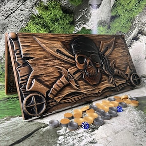 Könnte beinhalten: Ein Backgammon-Brett aus Holz mit einem geschnitzten Piratenschädel-Design, gekreuzten Schwertern und einer Windrose. Enthält Holzspielsteine und blaue Würfel. Das Brett ist braun mit detaillierter, strukturierter Oberfläche.