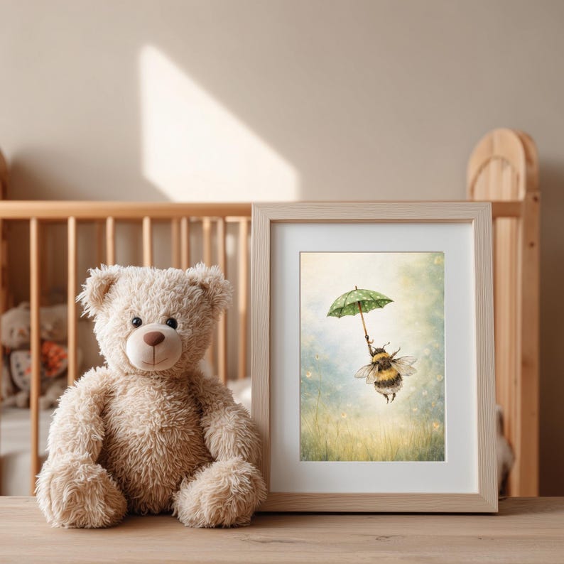 K&ouml;nnte beinhalten: Ein gerahmter Kunstdruck mit einer skurrilen Illustration einer Hummel, die einen gr&uuml;nen Regenschirm mit Tupfen h&auml;lt, vor einem weichen, vertr&auml;umten Hintergrund. Ein Teddyb&auml;r sitzt neben dem gerahmten Kunstdruck. Das Kunstwerk ist in einem hellen Holzrahmen.
