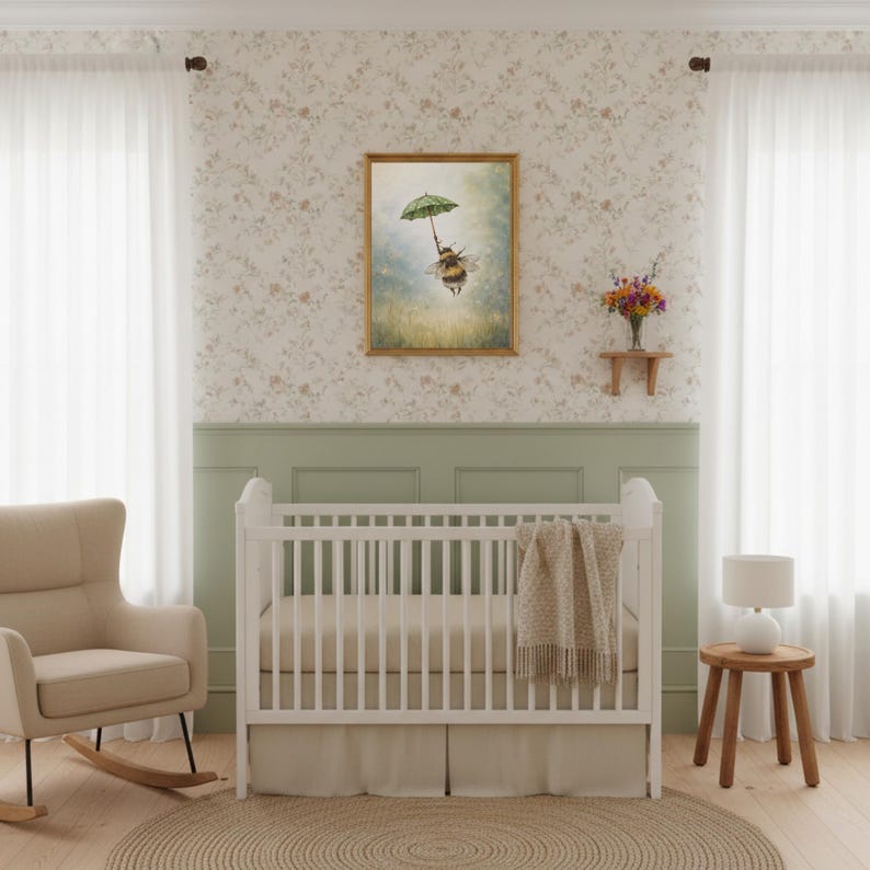 K&ouml;nnte beinhalten: Ein Kinderzimmer mit einem wei&szlig;en Kinderbett und einem beigen Teppich. Ein gerahmtes Bild einer Biene mit einem Regenschirm h&auml;ngt an der Wand. Ein beiger Schaukelstuhl und ein kleiner Beistelltisch aus Holz mit einer Lampe sind ebenfalls zu sehen.
