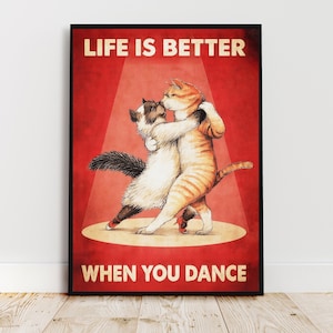 Puede incluir: Un póster enmarcado con el texto "LIFE IS BETTER WHEN YOU DANCE". La imagen presenta dos gatos bailando en un escenario. Uno es naranja y blanco, el otro negro y blanco. Ambos gatos llevan zapatos rojos.