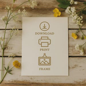 May include: A cream-colored card with the words "DOWNLOAD", "PRINT", and "FRAME" in brown, along with corresponding icons. The card is surrounded by white and yellow flowers, set against a light-colored wooden background.