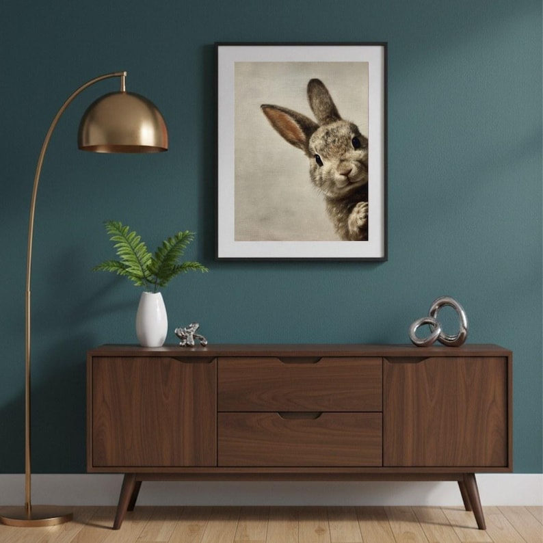 May include: A framed print of a rabbit peeking from the side. The artwork is displayed above a mid-century modern style wooden cabinet. A gold floor lamp and decorative items complete the room's decor.