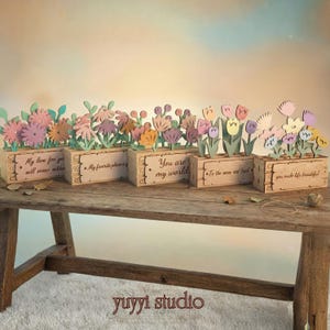 Peut inclure: Plusieurs bo&icirc;tes &agrave; fleurs en bois avec des fleurs d&eacute;coup&eacute;es au laser de diff&eacute;rentes couleurs, notamment du rose, du violet et du jaune. Chaque bo&icirc;te porte une inscription diff&eacute;rente : &laquo;&nbsp;My love for you will never wither&nbsp;&raquo;, &laquo;&nbsp;My favorite place is&nbsp;&raquo;, &laquo;&nbsp;You are my world&nbsp;&raquo;...