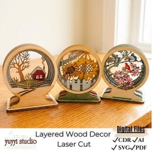 Könnte beinhalten: Drei geschichtete Holzdekorationen mit kreisförmigen Rahmen. Eines zeigt ein rotes Haus, ein anderes Sonnenblumen und das letzte einen Vogel auf einem blühenden Ast. Der Text lautet "Layered Wood Decor Laser Cut" und "Digital Files".