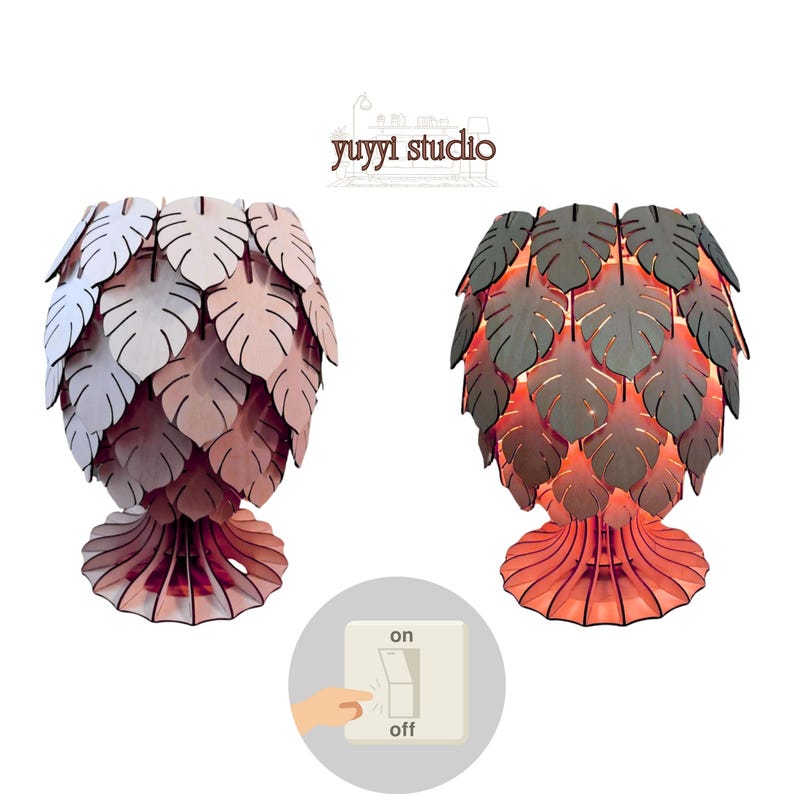 May include: Two wooden table lamps with leaf-shaped shades. One lamp is off, showing light pink and white leaves, while the other is on, with gray leaves and a warm orange glow. The base of each lamp is a matching color. The image includes a switch graphic.