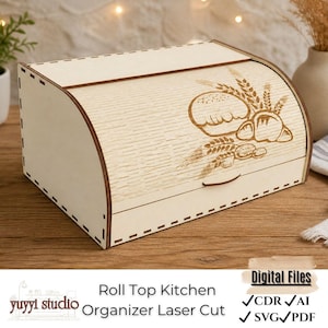 Op de afbeelding: Een lichtgekleurde houten broodtrommel met een rolblad en een lasergesneden ontwerp van brood en tarwe. De broodtrommel heeft een gebogen bovenkant en een handgreep. De tekst "Roll Top Kitchen Organizer Laser Cut" is zichtbaar.