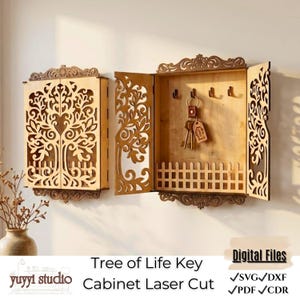 May include: A wooden key cabinet with a laser-cut tree of life design. The cabinet has a light brown finish and features a small fence detail at the bottom. The cabinet is open, revealing hooks for keys. The text "Tree of Life Key Cabinet Laser Cut" is visible.