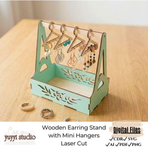 Puede incluir: Un expositor de pendientes de madera verde menta con mini perchas, diseño cortado con láser. El expositor contiene varios pendientes. La base tiene un diseño floral. El texto de la imagen dice "Wooden Earring Stand with Mini Hangers Laser Cut".