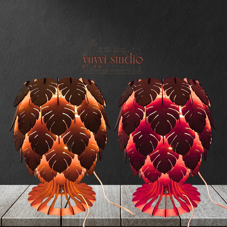 May include: Two wooden table lamps with leaf-shaped cutouts. One lamp is brown and orange, the other is red. The lamps have a unique design, with the text "yuyyi studio" in the background.