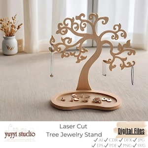 Puede incluir: Un expositor de joyas de árbol de madera cortada con láser. El soporte presenta un diseño en forma de árbol con ramas para colgar collares y pulseras. La base tiene una pequeña bandeja para anillos y pendientes.