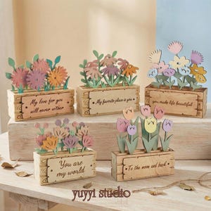Peut inclure: Plusieurs d&eacute;corations de bo&icirc;tes &agrave; fleurs en bois avec des fleurs d&eacute;coup&eacute;es au laser de diff&eacute;rentes couleurs. Chaque bo&icirc;te porte une citation inspirante, comme "You make life beautiful". Les bo&icirc;tes sont dispos&eacute;es sur une surface en bois.