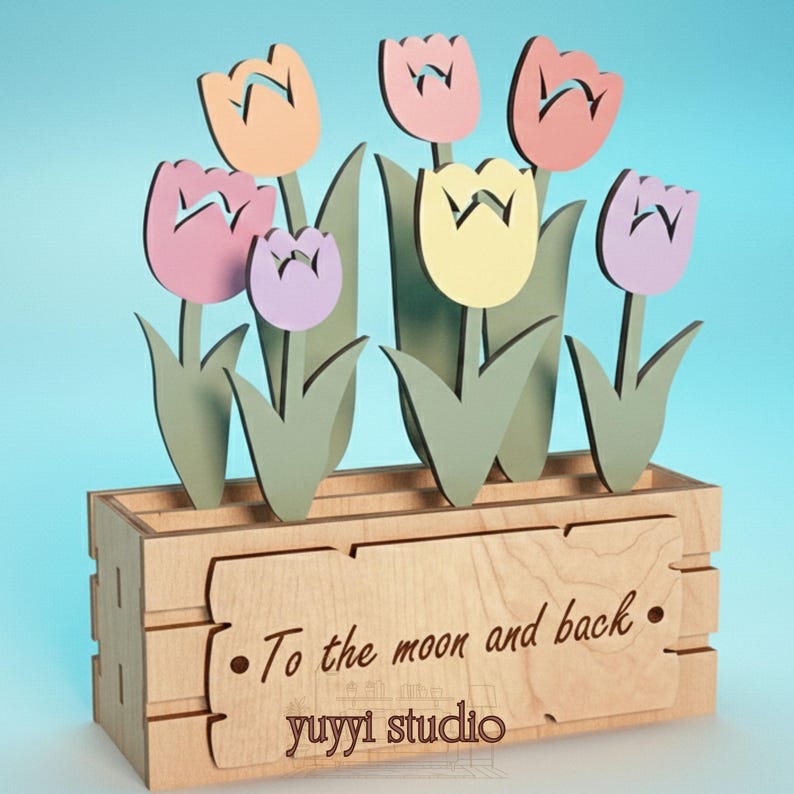 Peut inclure: Bo&icirc;te &agrave; fleurs en bois avec des tulipes aux couleurs pastel. La bo&icirc;te a une finition en bois clair et porte l'inscription "To the moon and back" et "yuyyi studio". Les tulipes sont dans des tons de rose, p&ecirc;che et jaune.