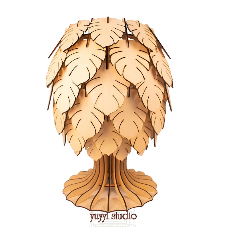 May include: A wooden lamp shaped like a tree, featuring a base, trunk, and a canopy of leaf-shaped cutouts. The lamp is made of light-colored wood and has a natural, organic aesthetic. The text "yuyyl studio" is visible at the base.