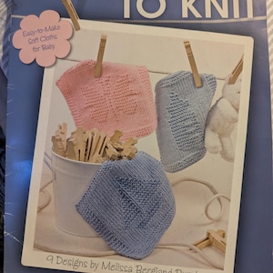 Op de afbeelding: Een boekomslag getiteld "baby washcloths TO KNIT" met drie gebreide babywaslappen in roze, blauw en lichtblauw, elk met een ander ontwerp. De omslag bevat ook de tekst "Easy-to-Make Soft Cloths for Baby".