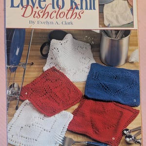 May include: A book cover titled "Love to Knit Dishcloths" by Evelyn A. Clark. The cover features several knitted dishcloths in red, white, and blue, with a close-up of a white knitted dishcloth. A fork and spoons are also visible.