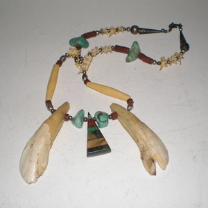 May include: A necklace made of bone, turquoise, and other stones. The necklace has a triangular pendant with a multi-colored stone.