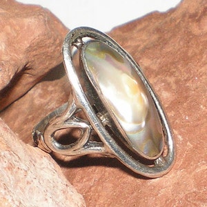 Könnte beinhalten: Ein silberner Ring mit einem ovalen, schillernden Abalone-Muschel-Stein, der in einem filigranen, durchbrochenen Design gefasst ist.