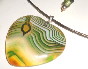 Puede incluir: Un collar con un colgante en forma de corazón de ágata verde y blanca. El colgante está unido a un cordón de cuero negro con un cierre plateado. El collar también incluye una cadena de plata con tres cuentas de vidrio verde.
