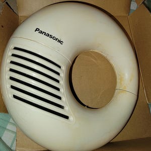 以下が含まれることがあります： 黒い水平通気孔が付いた、ドーナツ型の白いパナソニック製スピーカー。 スピーカーは段ボール箱に入っています。 「パナソニック」の文字がスピーカーに印刷されています。
