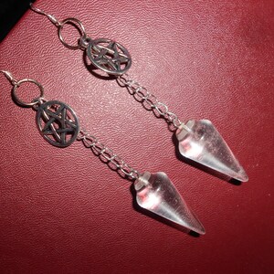 May include: A pair of silver earrings with a pentagram charm and a clear crystal pendulum. The earrings are hanging from a silver chain.