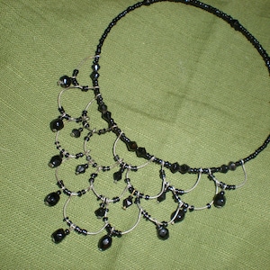 Puede incluir: Un collar de cuentas negras con un diseño de alambre plateado y cuentas negras colgantes.