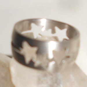 May include: A silver ring with three star cutouts. The ring is made of metal and has a polished finish.