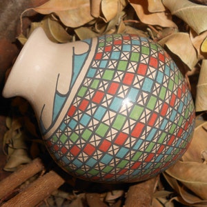 Może przedstawiać: Okrągły ceramiczny wazon z geometrycznym wzorem w odcieniach czerwieni, zieleni, błękitu i bieli. Wazon ma szeroki otwór i wąską szyjkę.