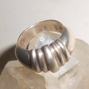 May include: A silver ring with a ridged, textured band. The ring is made of a smooth, polished metal.