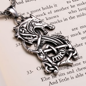 May include: Silver-toned wolf pendant necklace with intricate Celtic knot design. The pendant features a detailed wolf head and a complex interwoven pattern. The necklace is displayed on a book page.