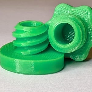 May include: Bright green 3D-printed bottle stopper set. The set includes a base, a threaded stopper, and a star-shaped top. The parts are designed to fit together. The stopper is made of plastic.