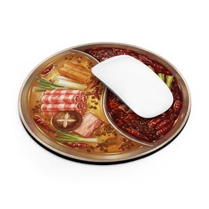 Könnte beinhalten: Ein rundes Mauspad mit einer Illustration eines geteilten Hot-Pot-Topfes, der eine goldene Brühe auf der einen und eine scharfe rote Chili-Brühe auf der anderen Seite zeigt, belegt mit rohem Fleisch, Pilzen und Frühlingszwiebeln, mit weißer Maus.