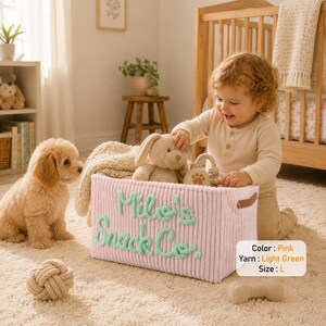 May include: A rectangular pink corduroy storage bin featuring light green embroidered text that reads Milo's Snack Co. The bin includes brown side handles and is labeled with the text Color: Pink, Yarn: Light Green, Size: L.