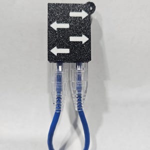 May include: A black plastic box with three white arrows pointing upwards. Two blue ethernet cables are connected to the box.