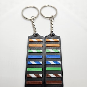 May include: Two keychains with black rectangular tags. Each tag has a series of colorful horizontal bars: orange and white, green and white, blue and white, green, and brown and white. The keychains have silver key rings and chains.