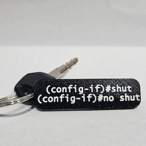 Puede incluir: Llavero negro con una llave plateada y una etiqueta negra que dice "(config-if)#shut (config-if)#no shut"