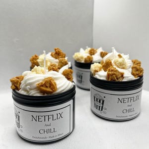Peut inclure: Quatre bougies à couvercle noir avec de la cire fouettée blanche, du pop-corn et des garnitures de couleur caramel. Chaque bougie porte une étiquette indiquant "Netflix and Chill" avec un graphisme de pop-corn. PetiteAmande - Made in Alsace est imprimé sur l'étiquette.