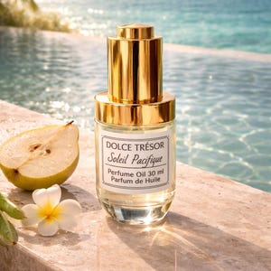 May include: A perfume oil bottle with a gold cap and label that reads "Dolce Trésor Soleil Pacifique". A pear half and a white flower are next to the bottle. The background is a pool and ocean.