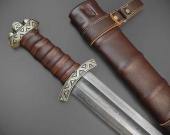 May include: A detailed image of a Viking sword with a brown leather-wrapped handle and a silver-colored guard. The blade is silver and the scabbard is brown leather with a strap and buckle.