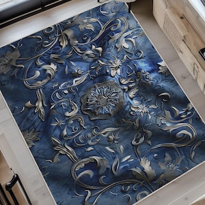 May include: An overhead shot of a blue and silver area rug with an ornate floral design. The rug features a central medallion and swirling patterns. The rug is placed in a well-lit entryway with a white chair and wooden accents.