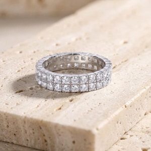 Op de afbeelding: Een zilverkleurige eternity ring met twee parallelle rijen heldere, rondgeslepen stenen in een metalen zetting. De ring heeft een doorlopend ontwerp van fonkelende stenen die de gehele omtrek van de band omsluiten.