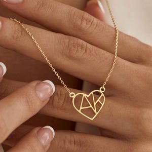 Peut inclure: Un collier doré avec un pendentif en forme de cœur au design géométrique ajouré. Le pendentif est suspendu à une fine chaîne à maillons délicats. La forme du cœur est divisée en segments angulaires, créant un aspect moderne et stylisé.
