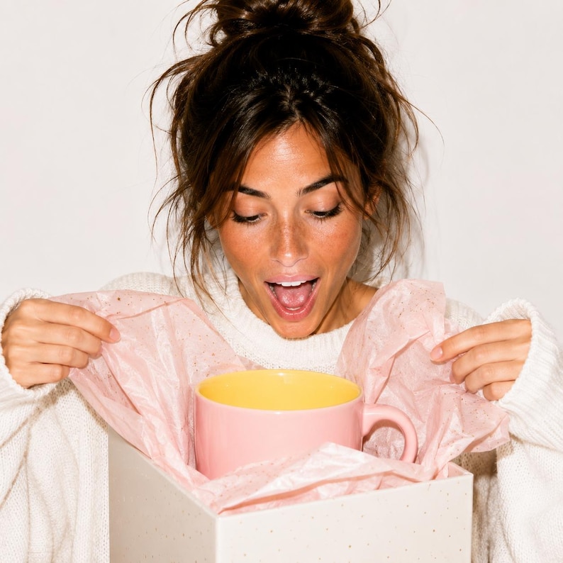 Peut inclure: Un mug en c&eacute;ramique avec un ext&eacute;rieur rose clair et un int&eacute;rieur jaune vif, plac&eacute; dans une bo&icirc;te cadeau blanche garnie de papier de soie rose clair froiss&eacute;. Le mug pr&eacute;sente une anse arrondie sur le c&ocirc;t&eacute; droit et une finition lisse et unie.
