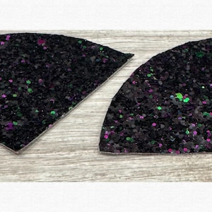 Può includere: Due pezzi neri a forma di ventaglio glitterato con macchie verdi e viola. Un pezzo è triangolare, l'altro è un semicerchio. Un righello blu è accanto al semicerchio. I pezzi sono su una superficie di legno chiaro.