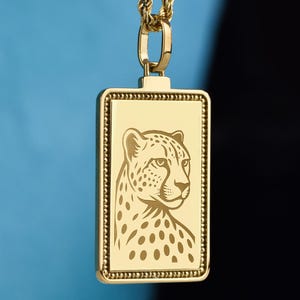 以下が含まれることがあります： ヒョウのデザインが施された、金色の長方形ペンダントネックレス。ペンダントは、お揃いの金のロープチェーンから吊り下げられています。ヒョウの頭部は横顔で描かれており、詳細な斑点と顔の特徴が表現されています。