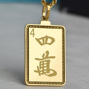 May include: Gold-colored pendant necklace featuring a rectangular pendant with the number "4" and Chinese characters. The pendant is suspended from a gold rope chain. The pendant has a beaded border.